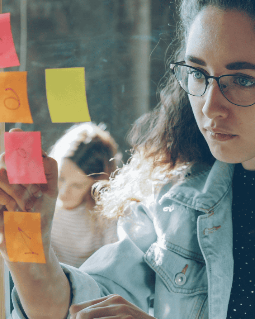 Frau schreibt an einer Glasscheibe mit Post-its, Business-Workshop.